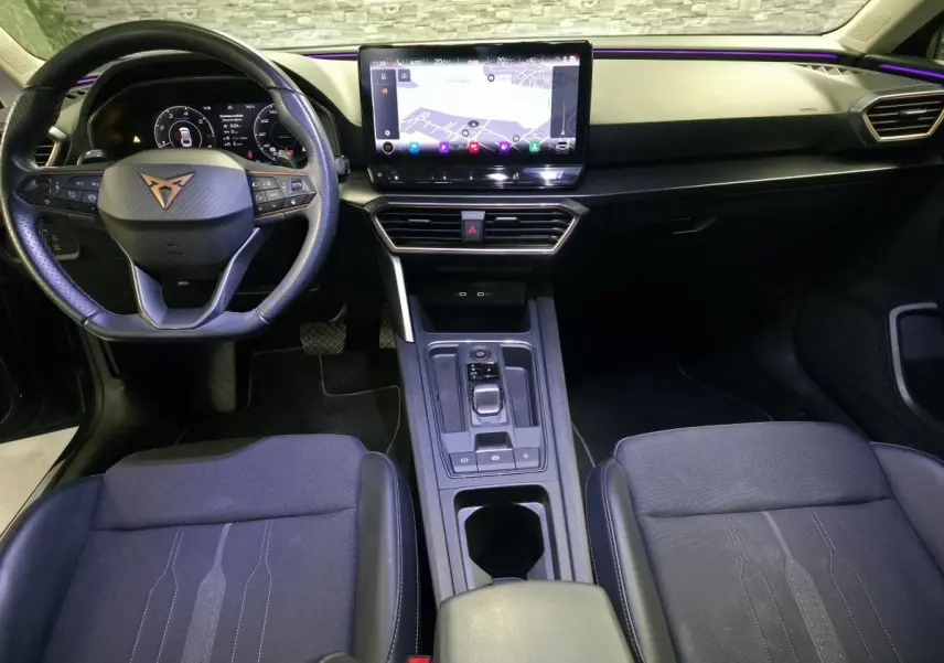 Vue intérieure avant de la CUPRA Leon Sportstourer 2024, volant cuir avec logo cuivre et écran tactile central lumineux.