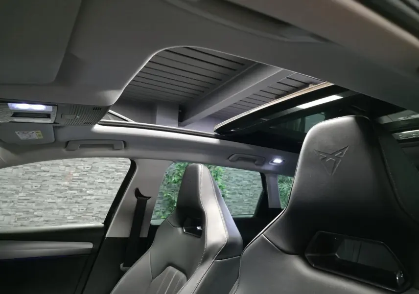 Vue intérieure avant du CUPRA Leon Sportstourer gris, sièges baquets noirs avec logo embossé et toit ouvrant panoramique.