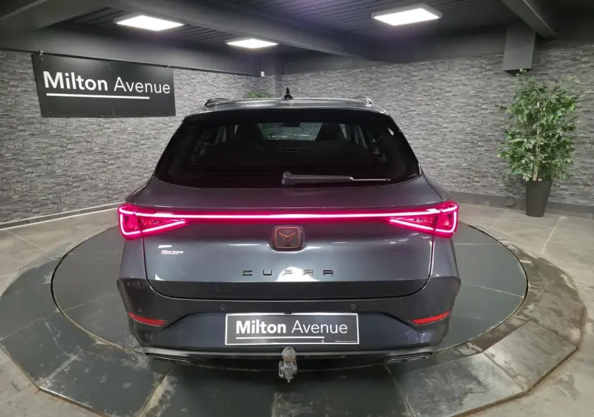 Vue arrière d'une CUPRA Leon Sportstourer gris magnétique avec feux LED allumés et crochet d'attelage escamotable visible.