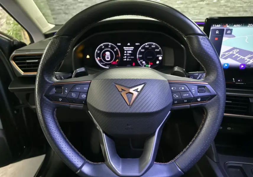 Vue rapprochée du volant cuir noir à surpiqûres copper de la CUPRA Leon 2024 avec tableau de bord digital et écran tactile.