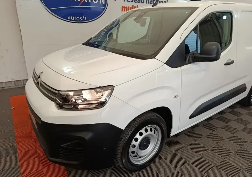 Vue 3/4 avant droite d’un Citroën Berlingo blanc avec pare-chocs noirs et jantes acier en intérieur showroom.