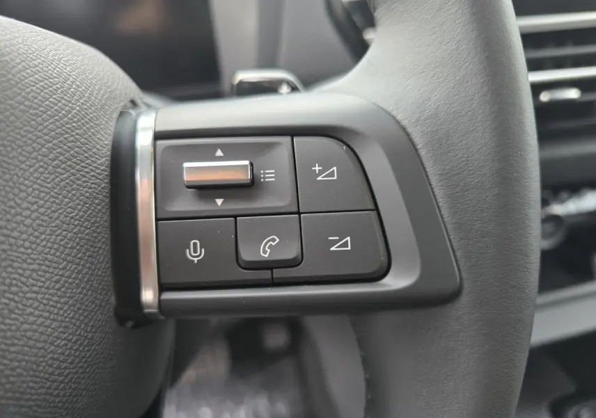 Gros plan sur les commandes vocales et téléphone au volant cuir noir de la Citroën C4 III hybride 2025.