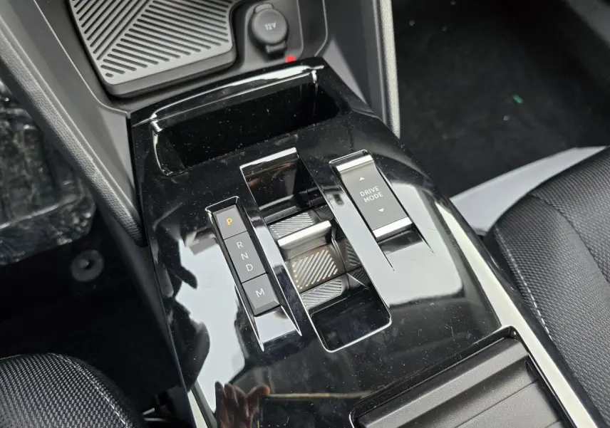 Gros plan sur la console centrale noire brillante avec commandes de boîte auto et mode de conduite de la Citroën C4 hybride.