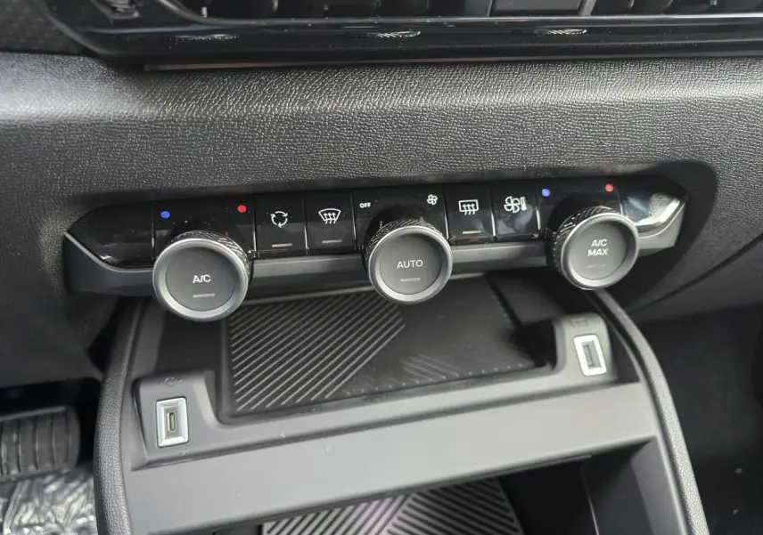 Vue rapprochée de la console centrale noire de la Citroën C4 hybride 2025, avec commandes climatisation et ports USB visibles.