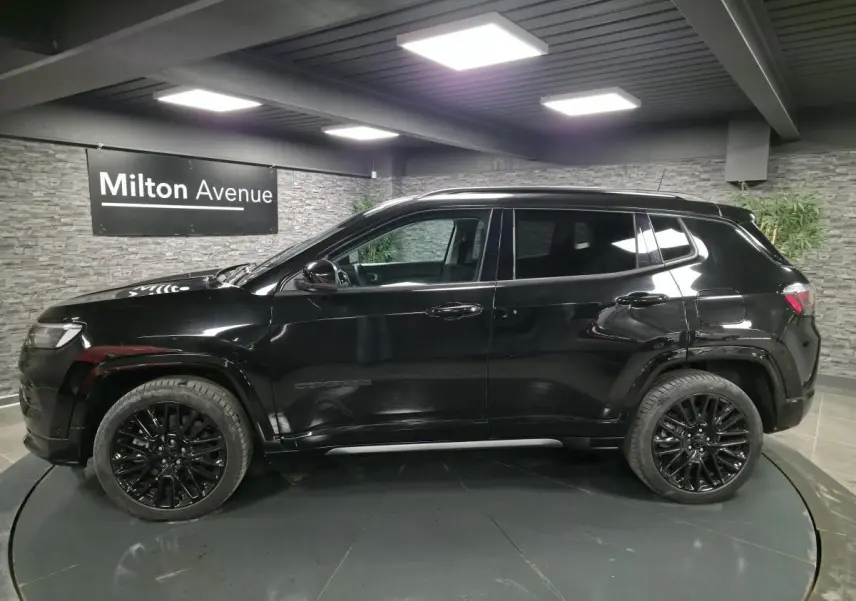 Profil côté gauche d'un Jeep Compass noir brillant avec jantes alliage noires dans un showroom intérieur.