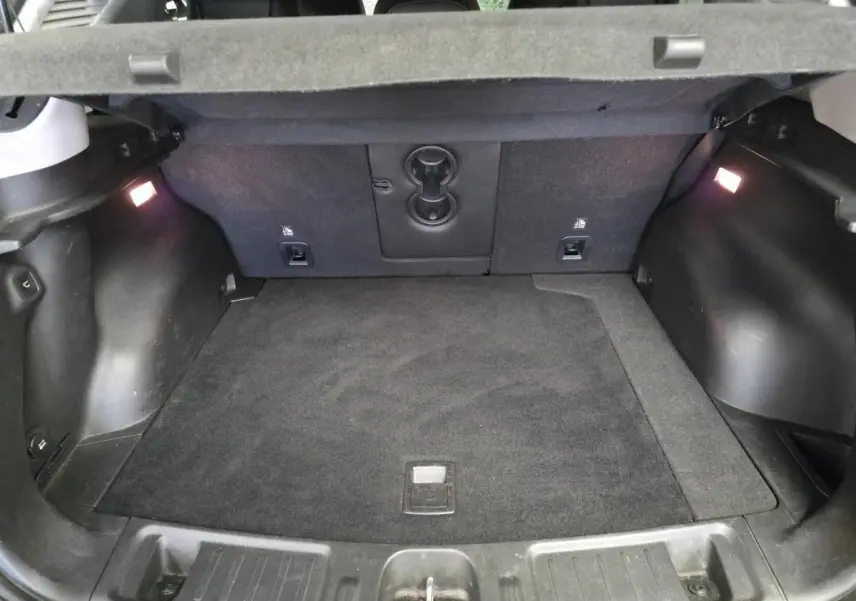 Coffre spacieux du Jeep Compass 2022 hybride rechargeable, vue de l'intérieur avec tapis noir et éclairage latéral.