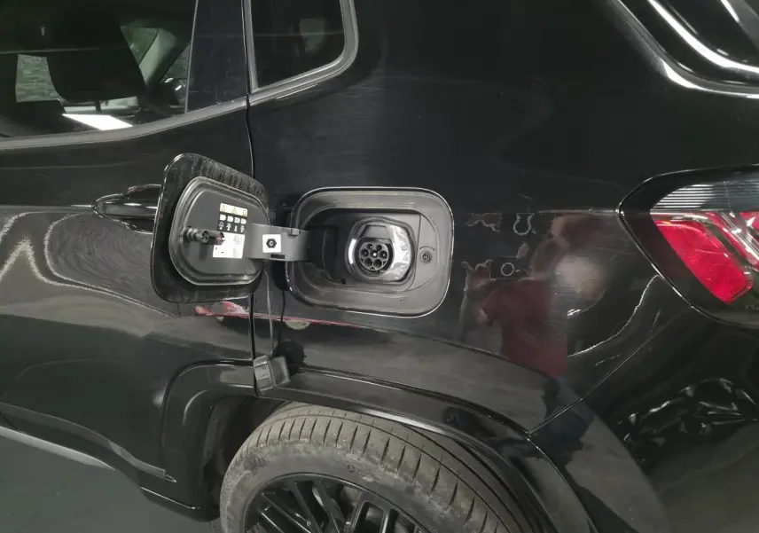 Prise de recharge ouverte côté gauche arrière d'un Jeep Compass noir, mettant en valeur la connectique hybride rechargeable.