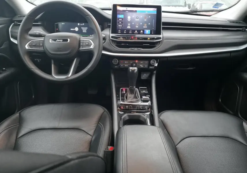 Intérieur du Jeep Compass 2022 en vue frontale, sièges cuir noirs et tableau de bord avec écran tactile central.