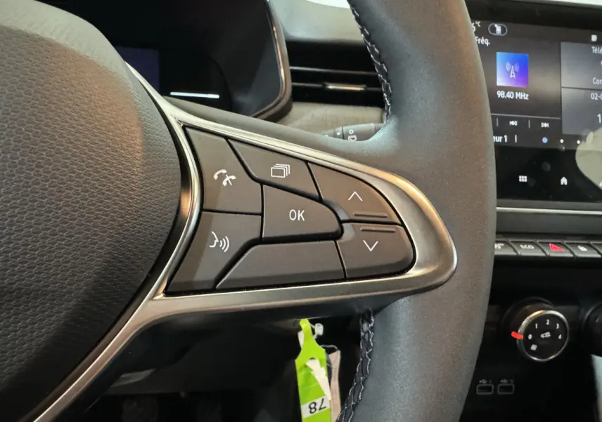Gros plan sur les commandes au volant cuir noir de la Renault Clio 2025 avec écran tactile en arrière-plan.