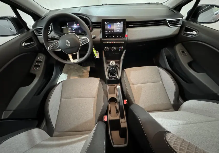 Vue intérieure avant de la Renault Clio 2025 avec sièges gris clair, volant multifonctions et écran tactile central.
