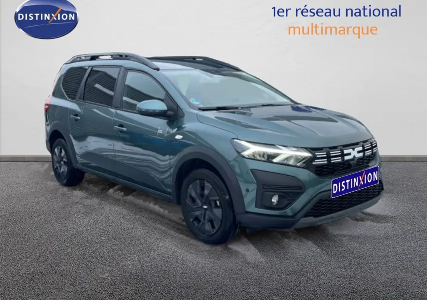 Dacia Jogger 2025 vert cèdre métal en 3/4 avant droit, avec jantes noires et toit barres de toit visibles.
