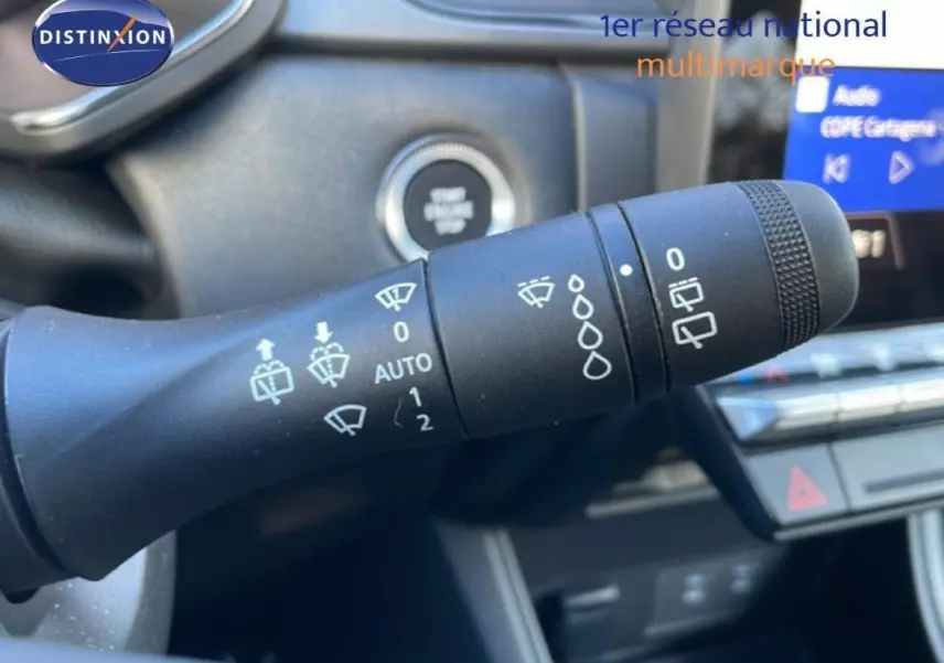 Gros plan sur la commande des essuie-glaces dans l’habitacle d’un Renault Captur rouge 2025, avec écran tactile en arrière-plan.