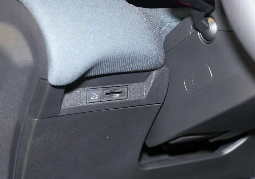 Gros plan sur le bouton d'ouverture du hayon sous le tableau de bord côté conducteur du Citroën C5 Aircross gris platinium.