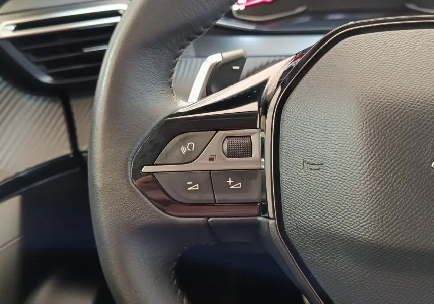 Gros plan sur le volant cuir noir multifonctions côté gauche du Peugeot 2008 blanc, avec commandes audio intégrées.