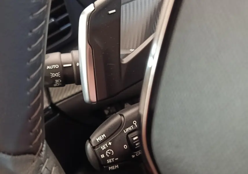 Gros plan sur le volant cuir noir de la Peugeot 2008 2021, montrant les commandes de régulateur de vitesse et éclairage.