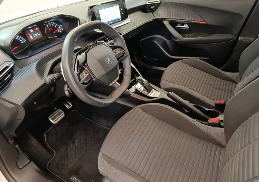 Vue intérieure côté conducteur du Peugeot 2008 2021, volant cuir multifonctions et sièges tissu gris avec surpiqûres rouges.