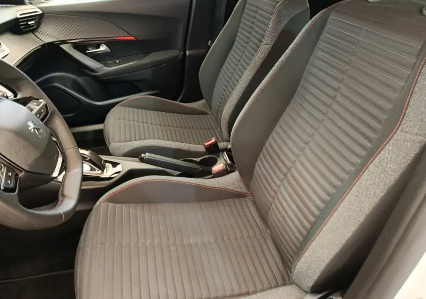 Vue intérieure côté conducteur du Peugeot 2008 blanc, sièges tissu gris avec surpiqûres rouges et volant cuir multifonctions.