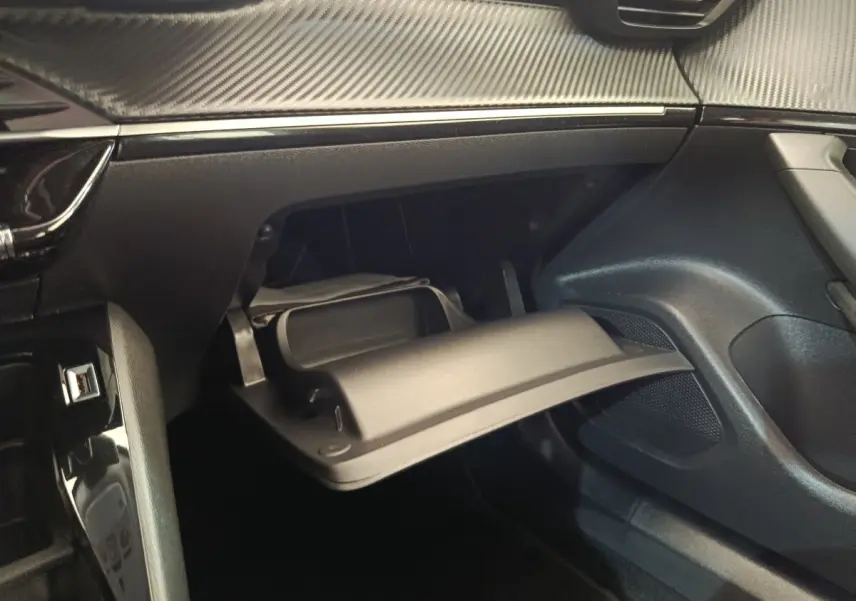 Intérieur de la Peugeot 2008 2021, vue du coffre à gants ouvert côté passager avec finition noire et détails carbone.