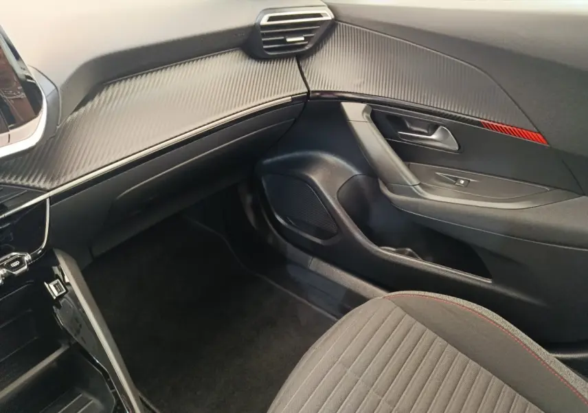 Vue intérieure côté passager du Peugeot 2008 blanc, avec tableau de bord noir et détails rouges sur la portière.