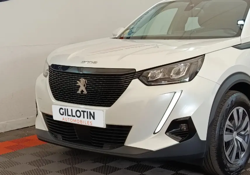 Vue 3/4 avant droit d’un Peugeot 2008 blanc avec calandre noire et feux LED verticaux allumés.