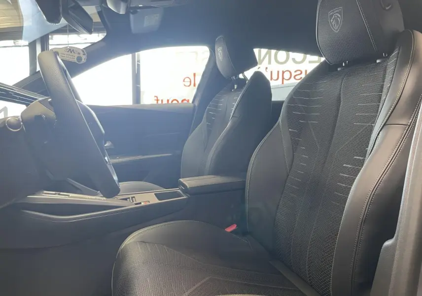 Vue intérieure côté gauche des sièges avant noirs avec surpiqûres vert Adamite et logo Peugeot brodé sur appuie-tête.