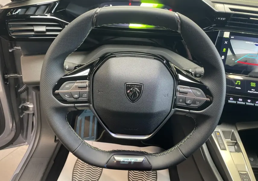 Vue rapprochée du volant GT en cuir noir avec surpiqûres vert Adamite de la Peugeot 308 Gris Artense 2026.