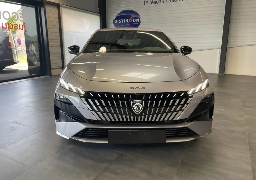 Vue frontale d'une Peugeot 308 gris Artense avec calandre noire brillante et logo lion lumineux en showroom.