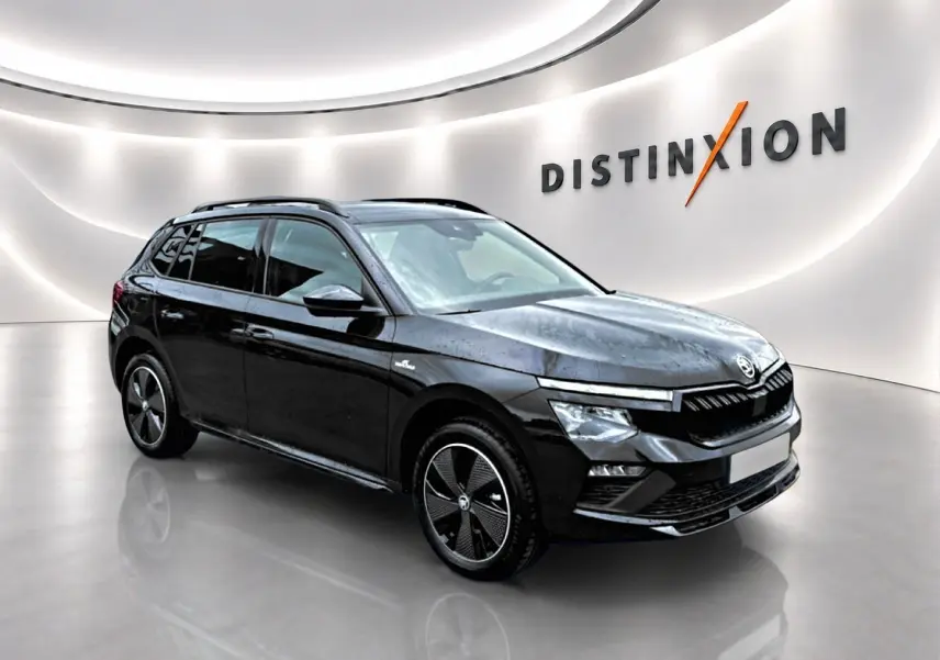 Vue 3/4 avant droite d'un Skoda Kamiq noir avec jantes alu noires, dans un showroom lumineux au mur blanc.
