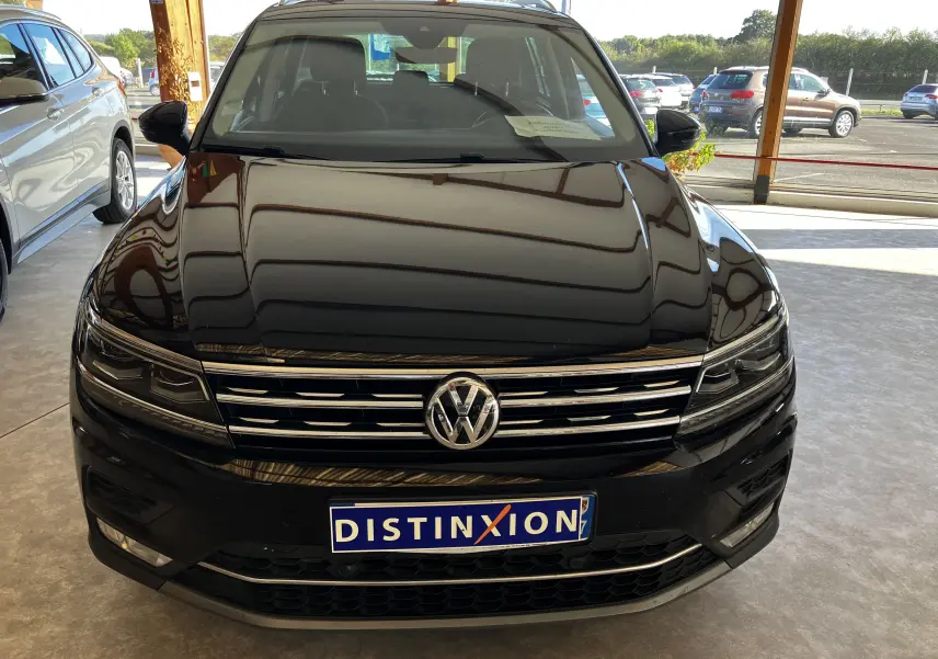 Vue frontale d'un Volkswagen Tiguan noir 2017 avec calandre chromée et plaque Distinxion en concession.