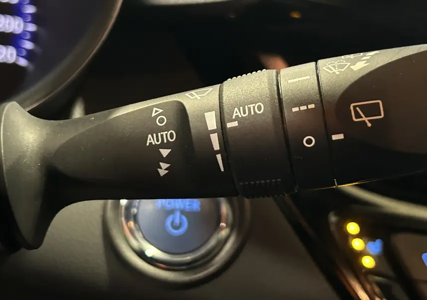 Gros plan sur la commande des essuie-glaces avec fonction auto, volant et bouton start du Toyota C-HR Hybride noir 2021.