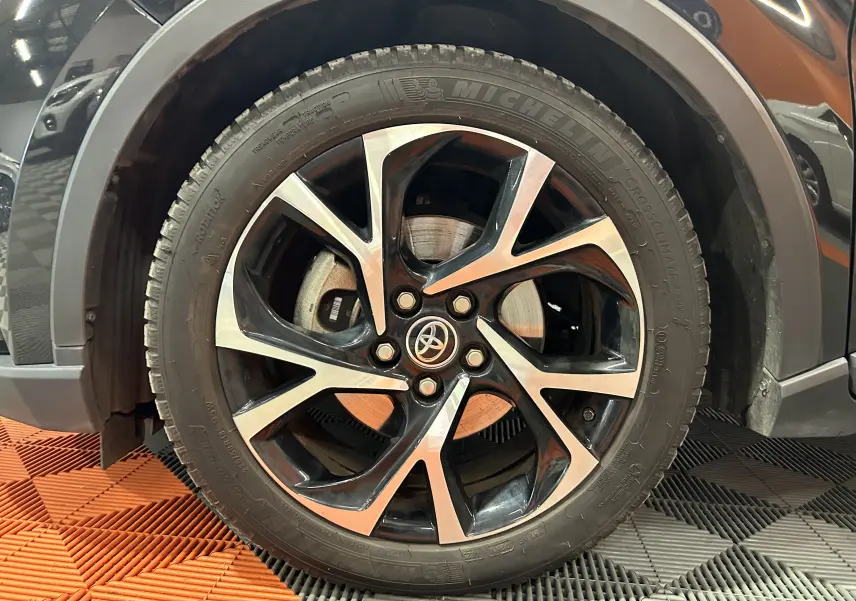 Gros plan sur la roue avant gauche noire métal du Toyota C-HR Hybride 122h Edition avec jante alliage bicolore.