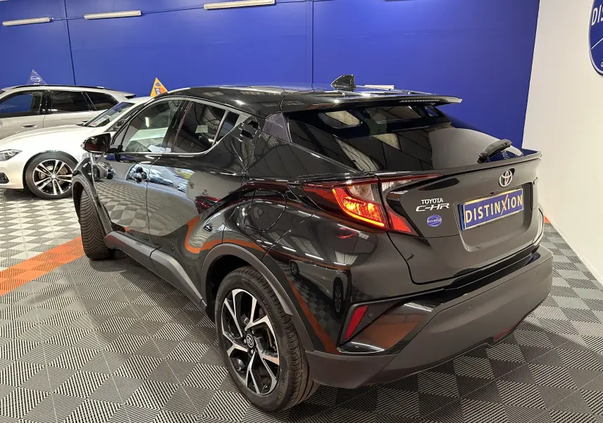 Toyota C-HR Hybride noir métal vu en 3/4 arrière droit dans un showroom avec jantes bi-ton et feux LED.