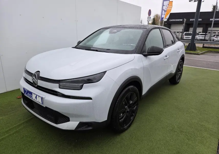 Citroën C4 III hybride blanc Okenite avec toit noir, vue 3/4 avant droit sur parking extérieur humide.