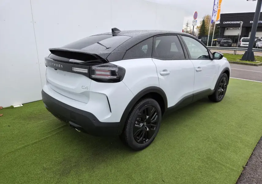 Vue 3/4 arrière droite d'une Citroën C4 blanche Okenite avec toit noir et jantes alliage noires sur pelouse verte.