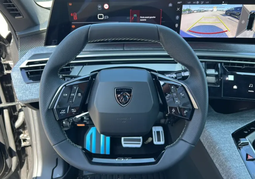 Vue rapprochée du volant cuir multifonctions Peugeot 3008 Hybrid GT 2025 avec tableau de bord digital et caméra de recul affichée.