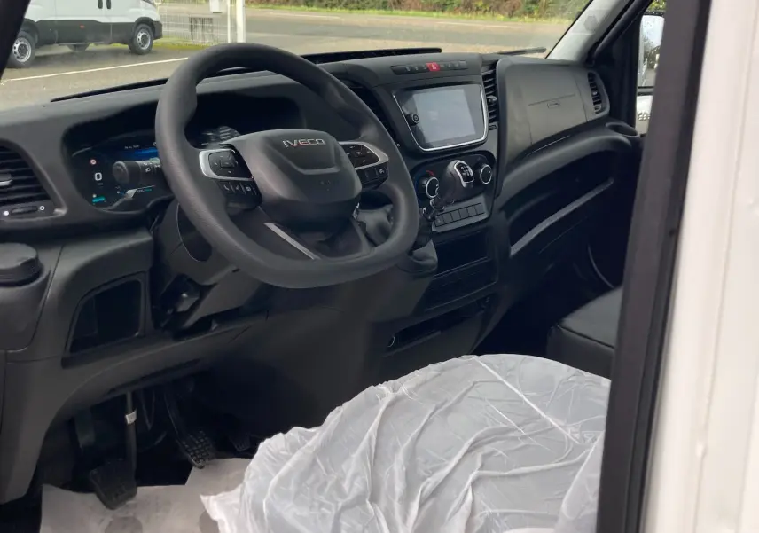 Vue intérieure côté conducteur de l'Iveco Daily blanc, montrant le volant, tableau de bord et levier de vitesses manuel.