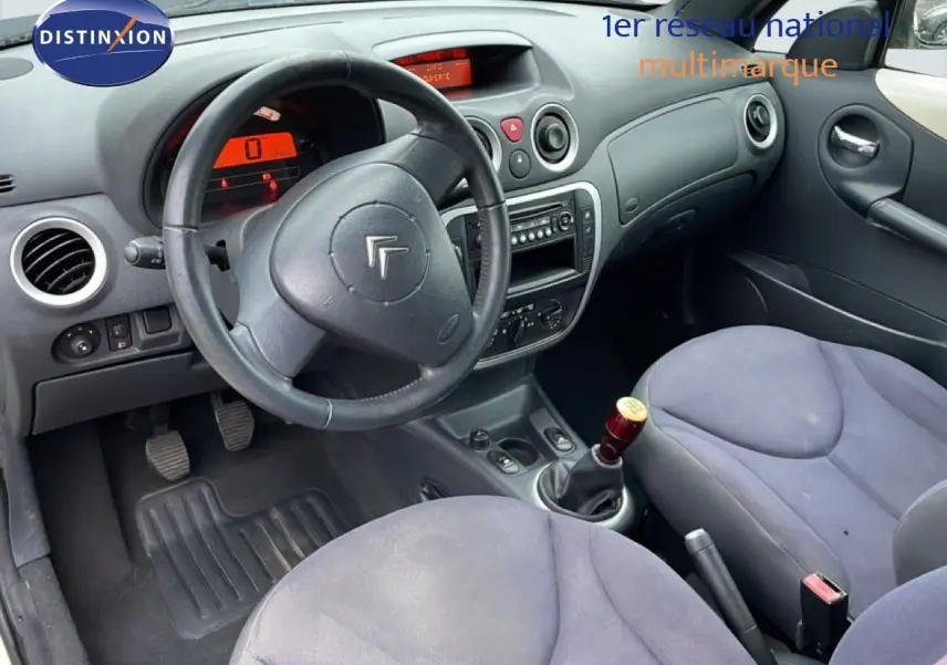 Vue intérieure côté conducteur de la Citroën C3 Pluriel 2007, volant cuir noir et sièges tissu gris bleu.