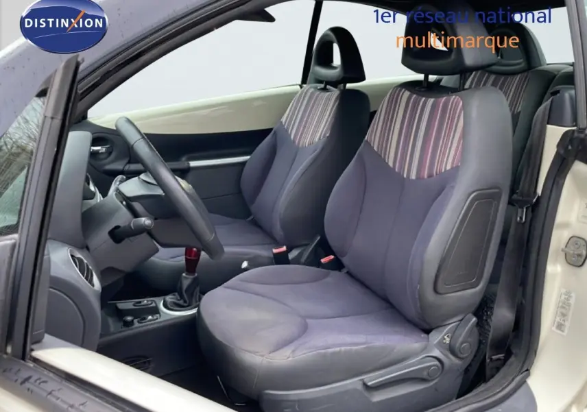 Vue intérieure côté gauche de la Citroën C3 Pluriel ivoire, sièges avant en tissu rayé noir et beige avec volant cuir.