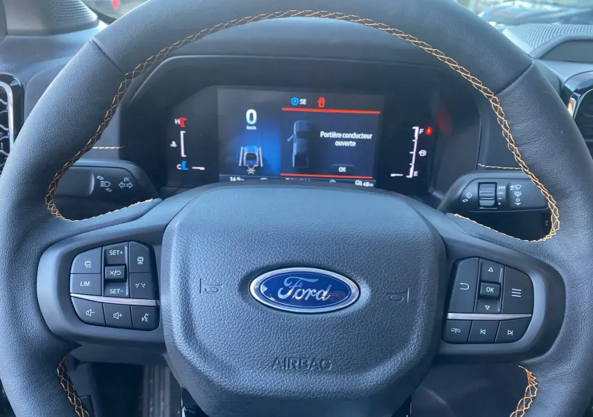 Vue rapprochée du volant en cuir noir avec surpiqûres orange du Ford Ranger 2025, tableau de bord digital allumé.