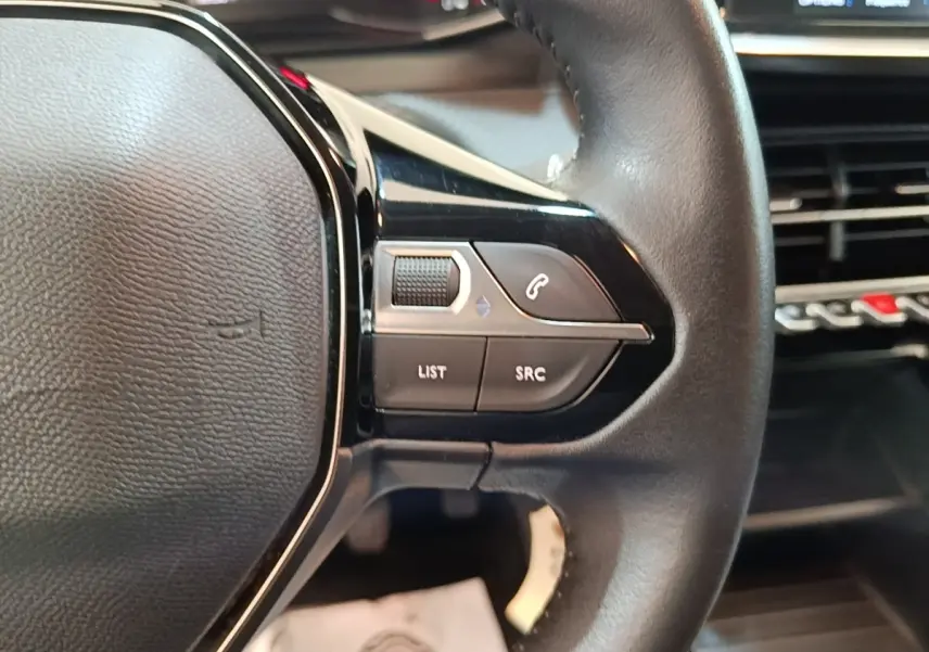 Gros plan sur le volant cuir multifonctions de la Peugeot 208 gris clair, avec commandes audio et téléphone intégrées.