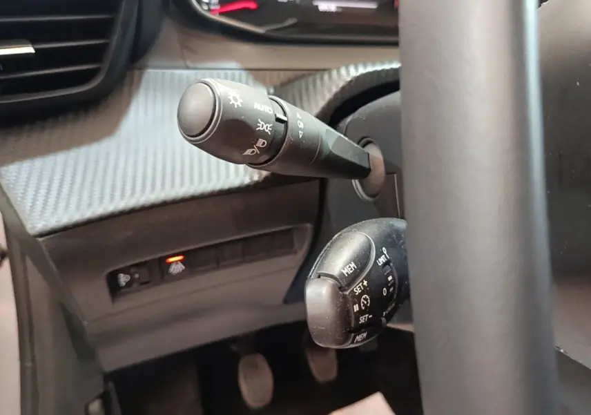 Gros plan sur les commandes au volant cuir de la Peugeot 208 gris clair, avec réglage régulateur de vitesse et éclairage automatique.