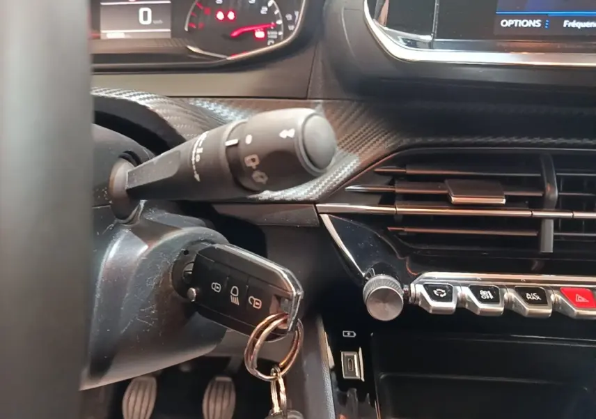 Gros plan intérieur sur le tableau de bord de la Peugeot 208 gris clair, clé insérée et commandes centrales visibles.
