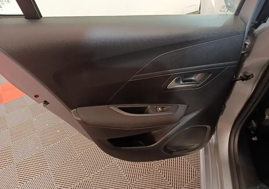 Vue rapprochée de la porte arrière droite grise claire du Peugeot 208 2023, avec poignée et commande de vitre noire.
