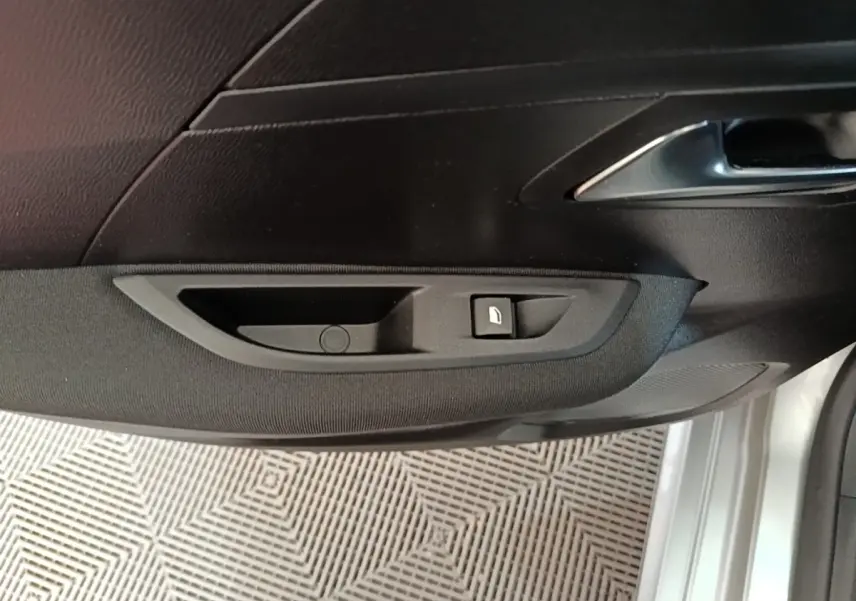 Détail de la porte avant gauche d’une Peugeot 208 gris clair, avec bouton de verrouillage et poignée intérieure chrome.