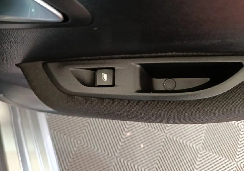 Détail de la commande de lève-vitre sur la porte intérieure côté conducteur d’une Peugeot 208 gris clair 2023.