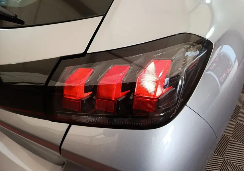 Gros plan sur le feu arrière droit rouge d’une Peugeot 208 gris clair, version PureTech 100 S&S Active Pack 2023.