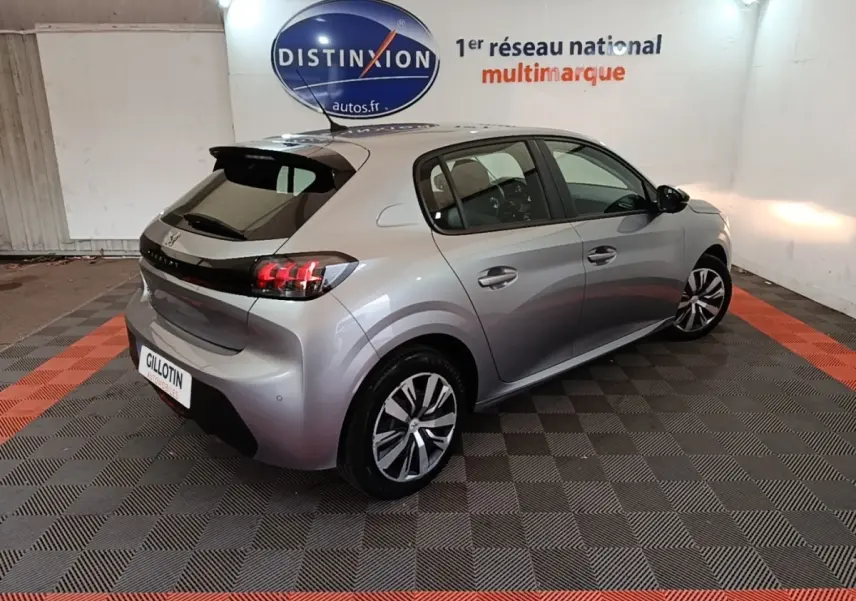 Peugeot 208 gris clair vue 3/4 arrière droit en intérieur, feux arrière LED et jantes alliage visibles.