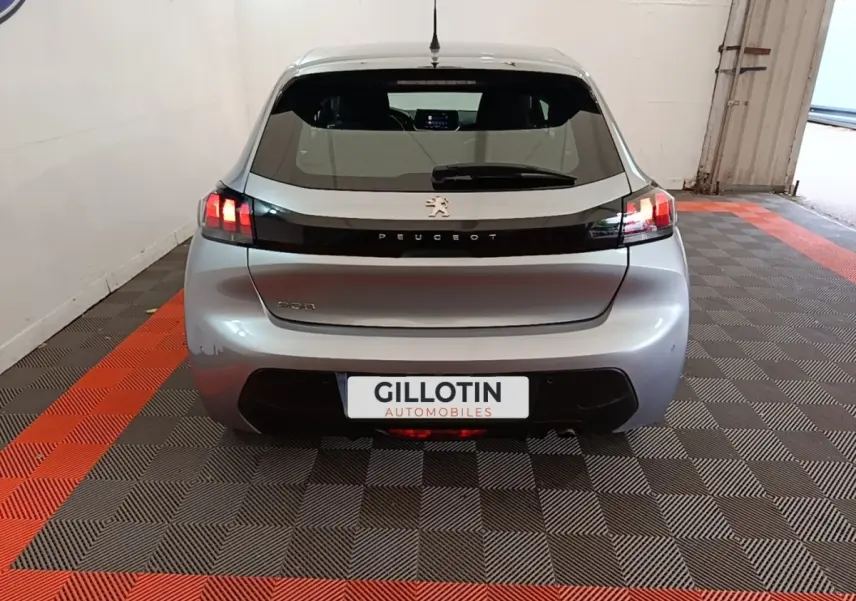Vue arrière d'une Peugeot 208 gris clair 2023 avec feux LED et logo Peugeot sur bande noire brillante.