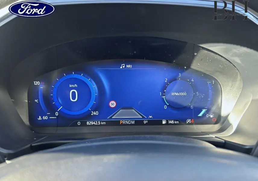 Vue rapprochée du tableau de bord numérique bleu du Ford Kuga 1.5 EcoBlue 2021, affichant vitesse, compte-tours et informations.