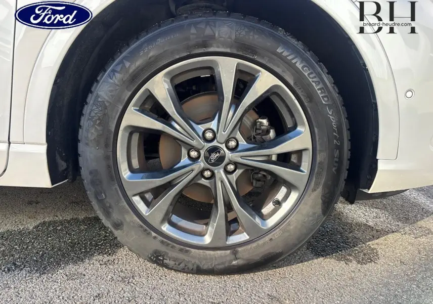 Gros plan sur la roue avant droite avec jante alliage gris du Ford Kuga blanc Premium Platinum.